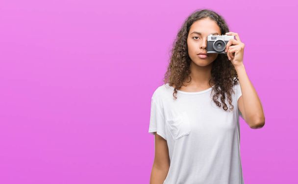 Young hispanic woman taking pictures using vintage camera with a confident expression on smart face thinking serious - Φωτογραφία, εικόνα
