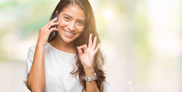 Young beautiful arab woman talking on the phone over isolated background doing ok sign with fingers, excellent symbol - Photo, Image