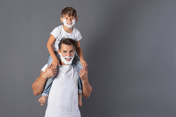Father and son with shaving foam on faces against color background. Space for text - Fotoğraf, Görsel