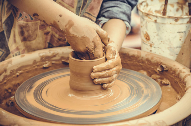 Hands of a potter. Potter making ceramic mug on the pottery wheel - Foto, imagen