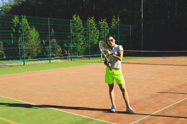 Retrato de chica con pelo de dardo jugar tenis. Pista de tenis de fondo.Polo camiseta blanca y pantalones cortos amarillos.Tiro deportivo
. - Foto, imagen