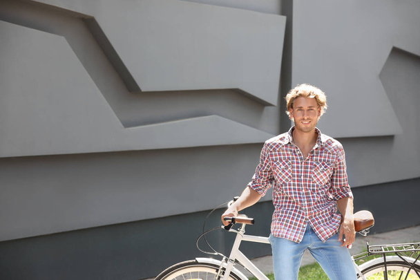 Bonito jovem com bicicleta perto de parede cinza ao ar livre. Espaço para texto
 - Foto, Imagem