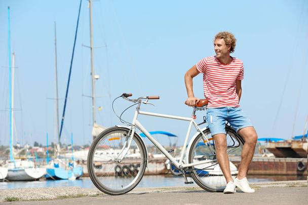 Handsome man with bicycle at pier on sunny day - Zdjęcie, obraz