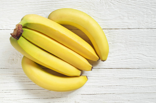 Joukko keltaisia banaaneja valkoisella puupohjalla, ylhäältä katsottuna kopiotilaa
 - Valokuva, kuva