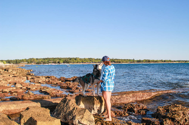 Αδριατική θάλασσα. Μεγαλόσωμος παίζουν στην παραλία πέτρες στη θάλασσα. Κορίτσι Παίξτε με σκύλο και τον τροφίμων. Treveling με σκύλο. Κροατία. - Φωτογραφία, εικόνα