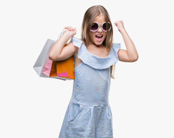 Jovem menina bonita segurando sacos de compras em vendas sobre fundo isolado irritado e frustrado gritando com raiva, louco e gritando com a mão levantada, conceito de raiva
 - Foto, Imagem