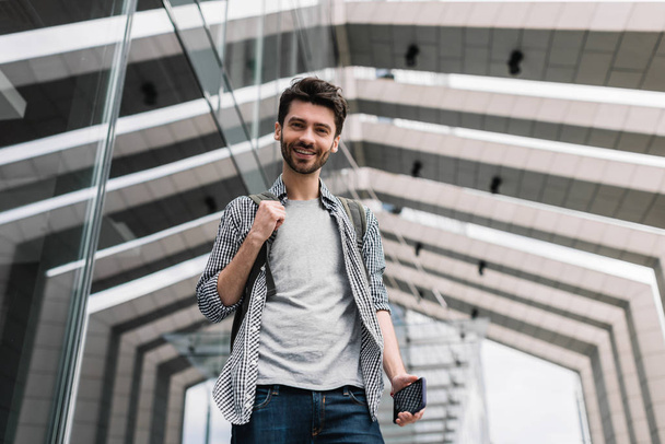 Portrait of happy smiling university students with backpack and smartphone going to take an exam. Bearded hipster wearing stylish casual clothes holding mobile in hand. - Foto, Imagem