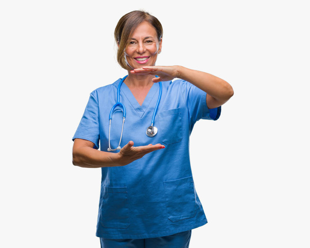 Medico infermiera anziana di mezza età donna su sfondo isolato gesticolando con le mani che mostrano segni di grandi e grandi dimensioni, simbolo di misura. Sorridendo guardando la telecamera. Concetto di misurazione
. - Foto, immagini