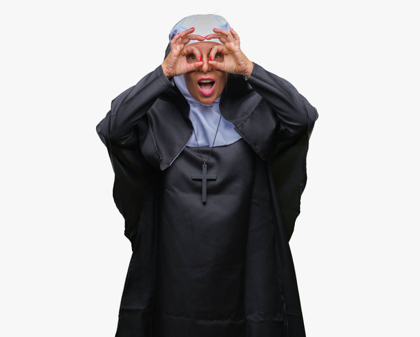 Middle age senior christian catholic nun woman over isolated background doing ok gesture like binoculars sticking tongue out, eyes looking through fingers. Crazy expression. - Photo, Image