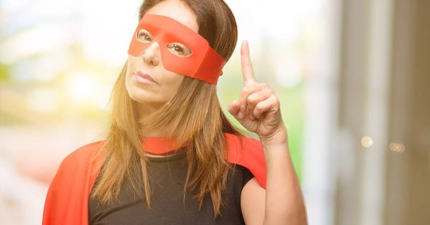 Супергероиня средних лет женщина в красной маске и плаще счастливый и удивленный аплодисменты выражая вау жест указывая вверх
 - Фото, изображение