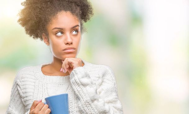 Mujer afroamericana joven goteando taza de café sobre fondo aislado cara seria pensando en la pregunta, idea muy confusa
 - Foto, imagen