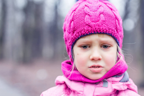 Porträt eines kleinen süßen kaukasischen Mädchens mit rosa Strickmütze, das weint, sich aufregt oder in einem Wald oder Stadtpark verliert . - Foto, Bild