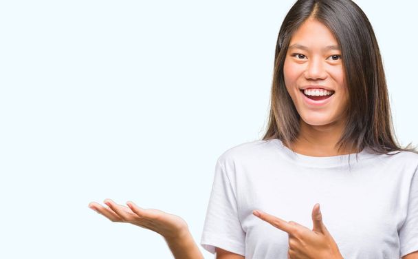 Jonge Aziatische vrouw over geïsoleerde achtergrond verbaasd en lachend naar de camera tijdens het presenteren met hand en met de vinger te wijzen. - Foto, afbeelding