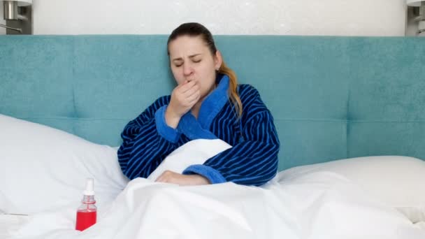 4 k wideo chore kobiety w szlafrok, leżąc w łóżku i rozpylanie medycyny w gardle - Materiał filmowy, wideo