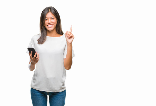 Giovane donna asiatica sms utilizzando smartphone su sfondo isolato sorpreso con un'idea o una domanda che punta il dito con la faccia felice, numero uno
 - Foto, immagini