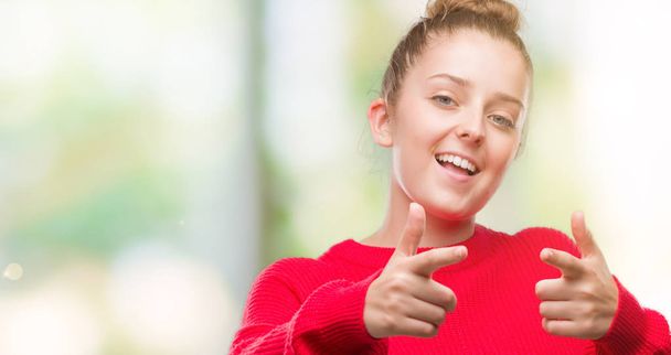 Giovane donna bionda che indossa panino e maglione rosso puntando il dito verso la fotocamera con viso felice e divertente. Buona energia e vibrazioni
. - Foto, immagini