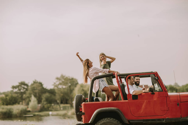 Happy friends having fun in convertible car at vacation by river - Photo, Image