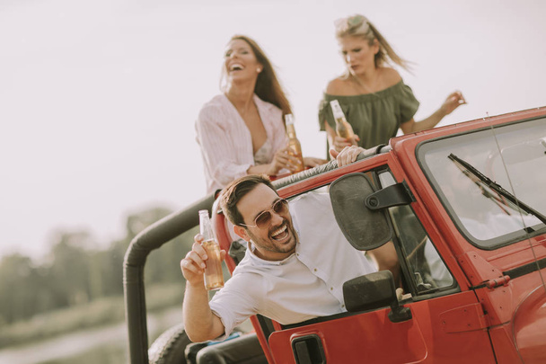 Young people having fun traveling together  in convertible car and drinking - Photo, Image