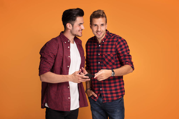 Happy young fashionable two men using smart phone at studio. - Фото, зображення