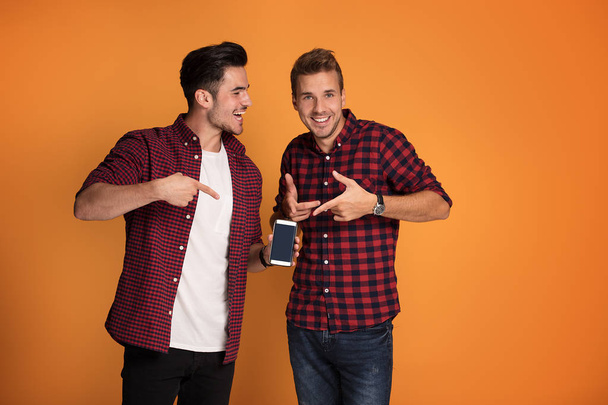 Happy young fashionable two men using smart phone at studio. - Zdjęcie, obraz