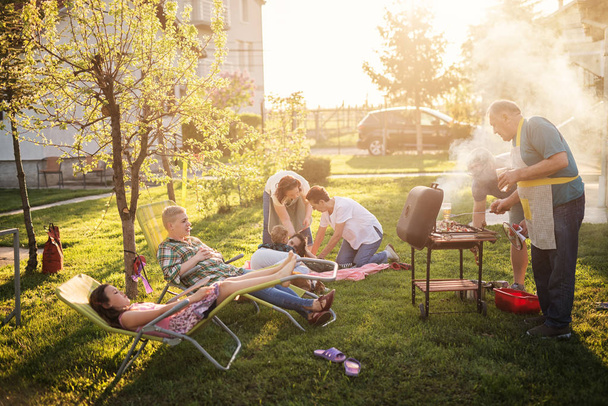 cheerful family cooking with outdoor grill at backyard on  sunny day - Fotografie, Obrázek