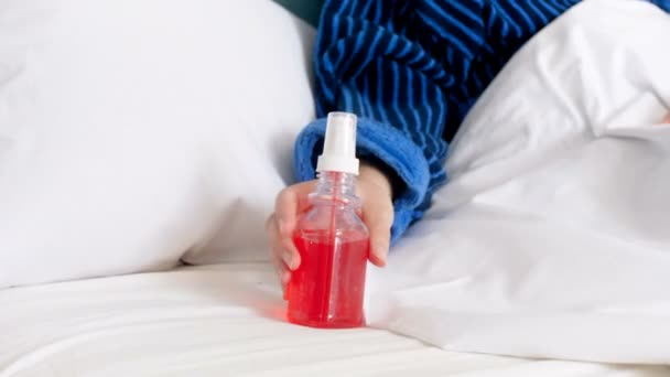 4k video of sick woman in bathrobe lying in bed and taking throat spray - Imágenes, Vídeo