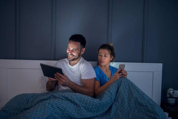Curieux jeune fille couchée dans le lit à côté de son petit ami jetant un oeil dans sa tablette copains secrètement
. - Photo, image