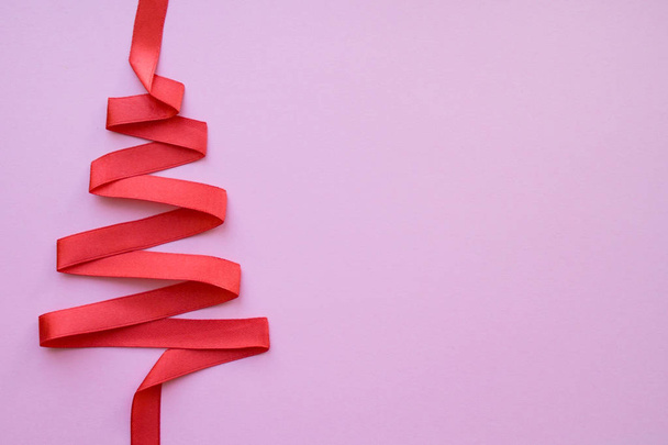 holidays, winter and celebration concept - Christmas and new year tree made from red ribbon on pink background free space for text - Photo, Image