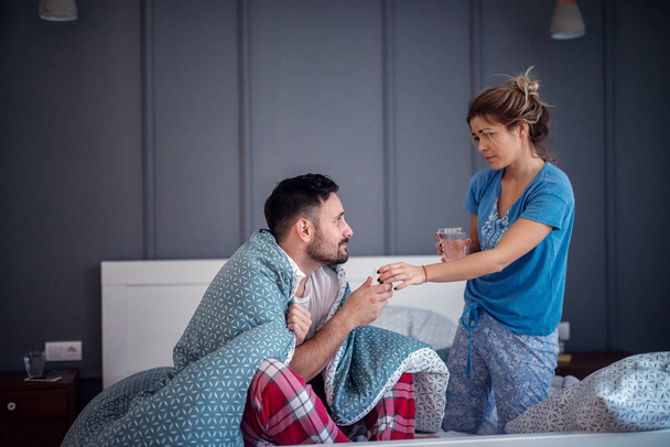 careful young woman bringing medications to ill boyfriend in bed - Foto, Imagem