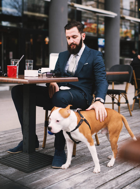 Бізнесмен у кав'ярні з собакою. Кращі друзі в кафе
.  - Фото, зображення