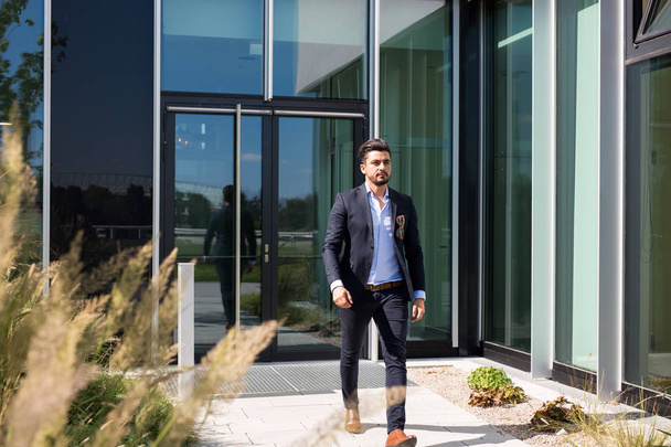 Handsome young businessman walking out of an office building being serious - Photo, Image