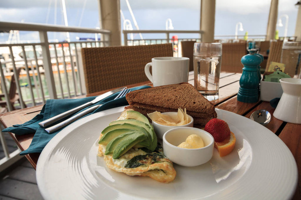 Ispanak, avokado dilimleri ve peynirle tost ve okyanusa bakan kahvaltı için tereyağı ile birlikte beyaz yumurta omlet. - Fotoğraf, Görsel