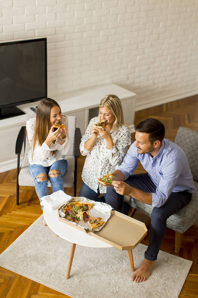 Маленькая группа молодых друзей, которые едят пиццу в комнате
 - Фото, изображение