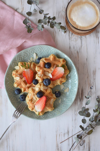 Belgische wafels gezond ontbijt concept blueberry aardbei Cappuccino koffie witte houten te achtergrond Eucalyptus tak bovenaanzicht plat leggen - Foto, afbeelding
