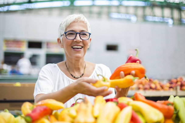 Портрет красивої старшої жінки в окулярах купує перець на ринку
 - Фото, зображення