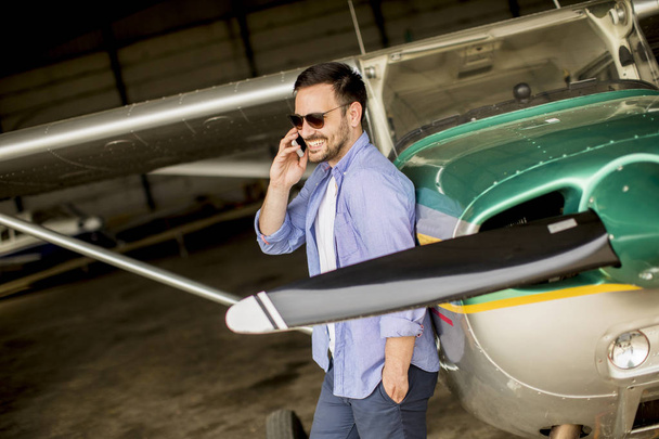 Joven piloto joven guapo comprobar avión en el hangar y el uso de teléfono móvil
 - Foto, imagen