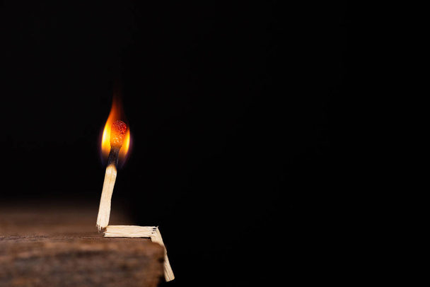 Hořící zápas člověka sedět na dřevěný stůl na tmavém pozadí. - Fotografie, Obrázek