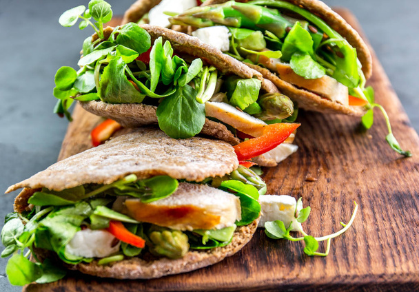 Pita sandwiches stuffed with chicken, vegetables and cheese on wooden cutting board. - Photo, image