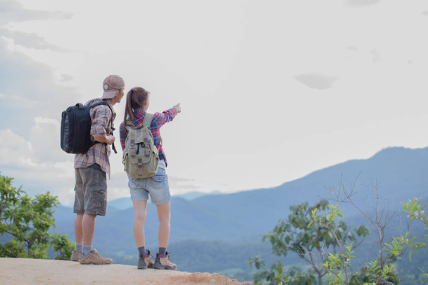 Hikers with backpacks relaxing on top of a mountain and enjoying the view of valley - 写真・画像