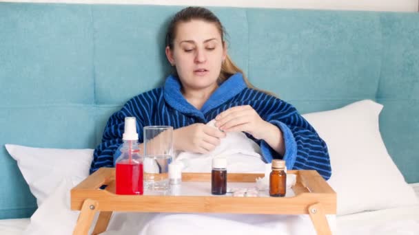 4 k Zdjęcia młoda kobieta mdłości leżąc w łóżku i używając wielu leków. Kobieta, stosowania aerozolu do nosa i gardła - Materiał filmowy, wideo