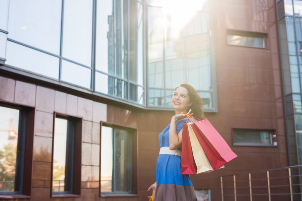 Einkauf, Rabatt- und Personenkonzept - Porträt einer jungen Frau im Kleid, die mit bunten Einkaufstaschen spaziert - Foto, Bild