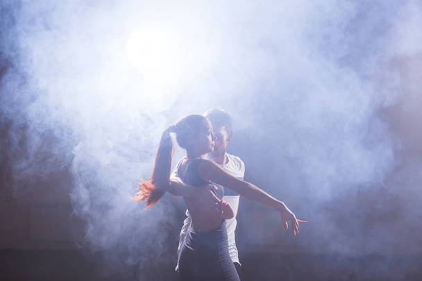 Bailarines hábiles actuando en la sala oscura bajo la luz del concierto y el humo. Pareja sensual realizando una danza contemporánea artística y emocional
 - Foto, imagen