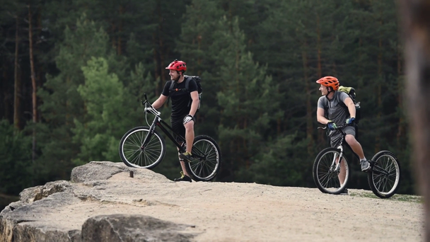trial bikers in helmets with bikes having conversation while standing on rock  in pine forest - Footage, Video