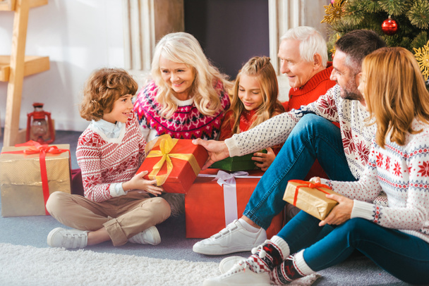 beautiful happy family with gift boxes sitting on floor of living room during christmas - Фото, изображение