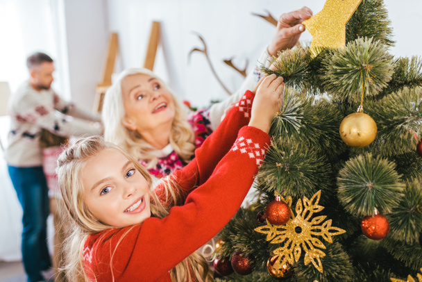 grandmother and granddaughter decorating christmas tree together - Fotoğraf, Görsel