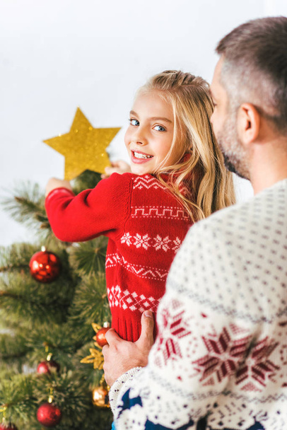 handsome young father carrying his daughter while she decorting christmas tree - Fotoğraf, Görsel