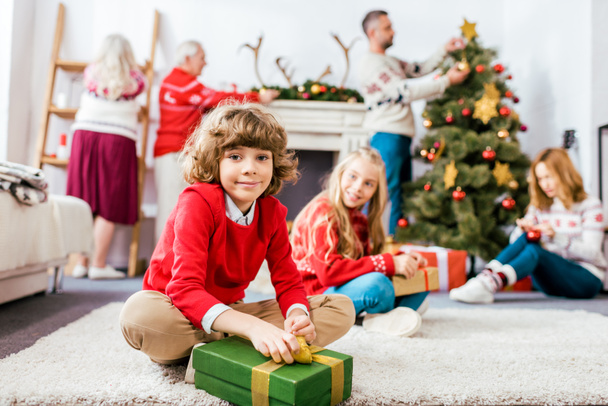 hymyilevät sisarukset istuvat lattialla yhdessä lahjojen kanssa jouluaattona
 - Valokuva, kuva