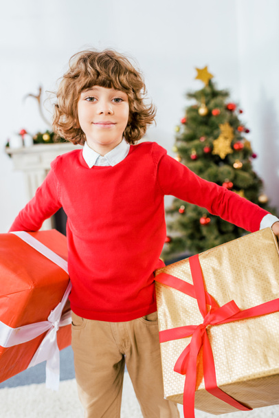 cute happy kid holding big christmas boxes and looking at camera - 写真・画像