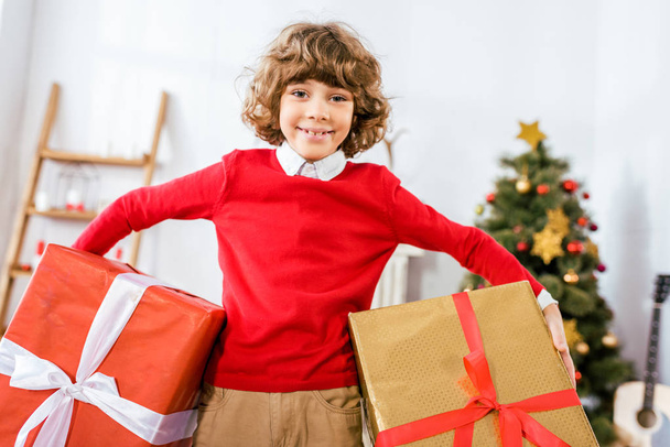 adorable happy kid holding big christmas boxes and looking at camera - Zdjęcie, obraz