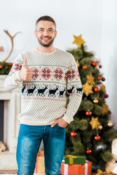 handsome bearded man in christmas sweater showing thumb up at camera - Foto, immagini